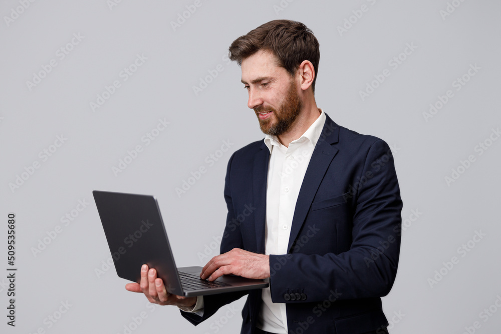 Handsome man in suit working online on laptop over grey studio background Handsome man in suit working online on laptop over grey studio background