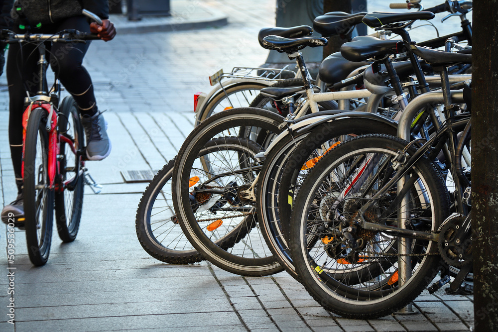 Bicycles stand in a row on a parking and one sportsman riding along the queue on a red bicycle