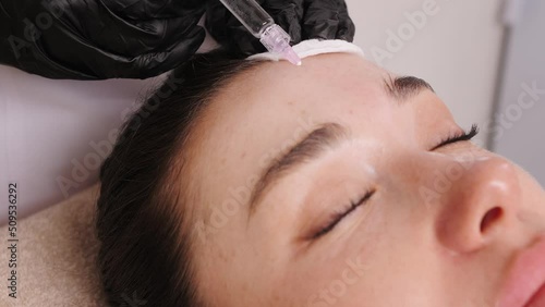 Doctor hands in black rubber gloves make neurotoxin injections in woman forehead at cosmetic procedure. Soft face skin of adult woman closeup photo