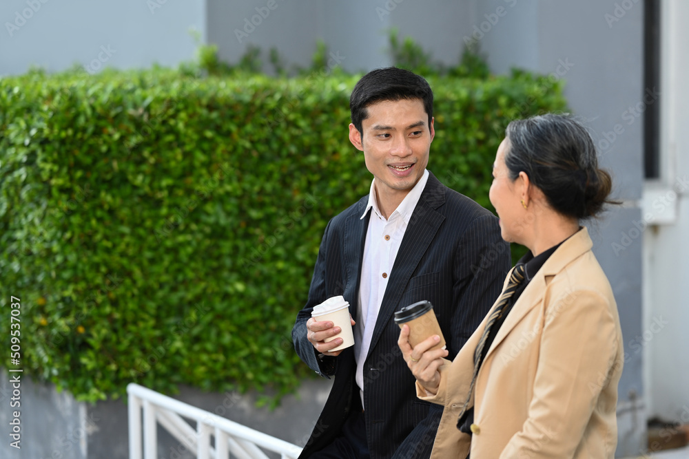 Friendly mature businesswoman and businessman having a discussion while taking coffee break at modern office district