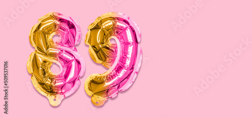 Rainbow foil balloon number, digit eighty nine on a pink background. Birthday greeting card with inscription 89. Top view. Numerical digit. Celebration event, template. Banner photo