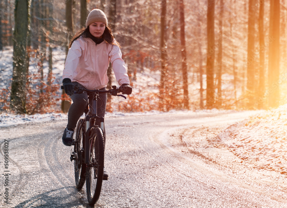 Obraz premium A woman rides a bike in winter. Concept of cycling during snowy weather. Snow and sun weather in the park
