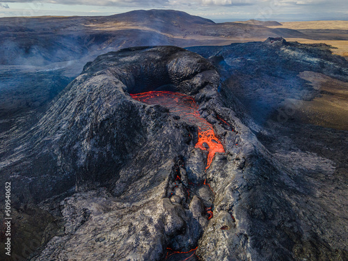 View into the crater of an active volcano with lava flow at the beginning of an eruption. Landscape on the Reykjanes Peninsula of Iceland. Puffs of smoke and steam around the crater