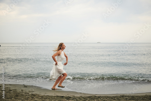 a girl in a white dress running on the beach