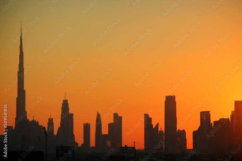 Orange sunset behind the Burj Khalifa and other buildings and towers in Dubai.