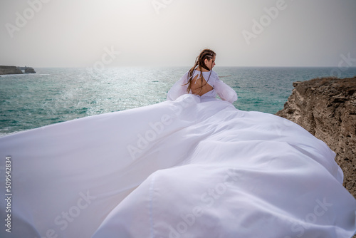 Happy freedom woman on the beach enjoying and posing in white dress. Rear view of a girl in a fluttering white dress in the wind. Holidays, holidays at sea.