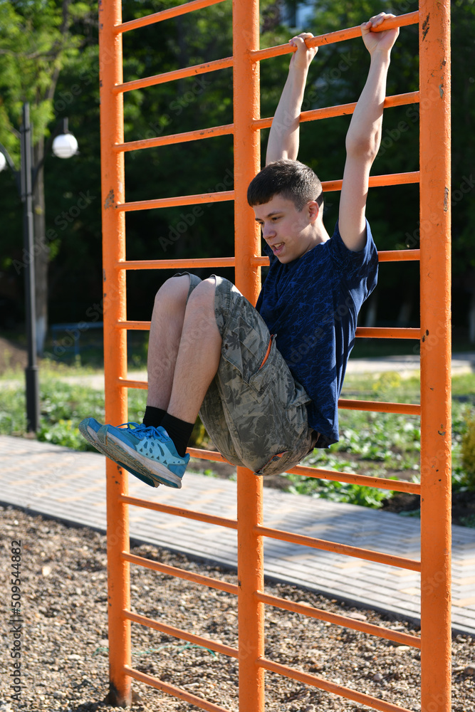 Fototapeta premium a teenage boy trains on a sports ground outdoors, he does physical exercises, a healthy lifestyle, a bright sunny day in summer