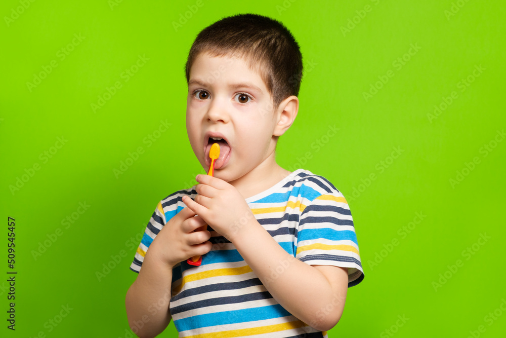 A preschool boy of 4 years cleans with a toothbrush a tongue on a green background. A preschool boy of 4 years cleans with a toothbrush a tongue on a green background.