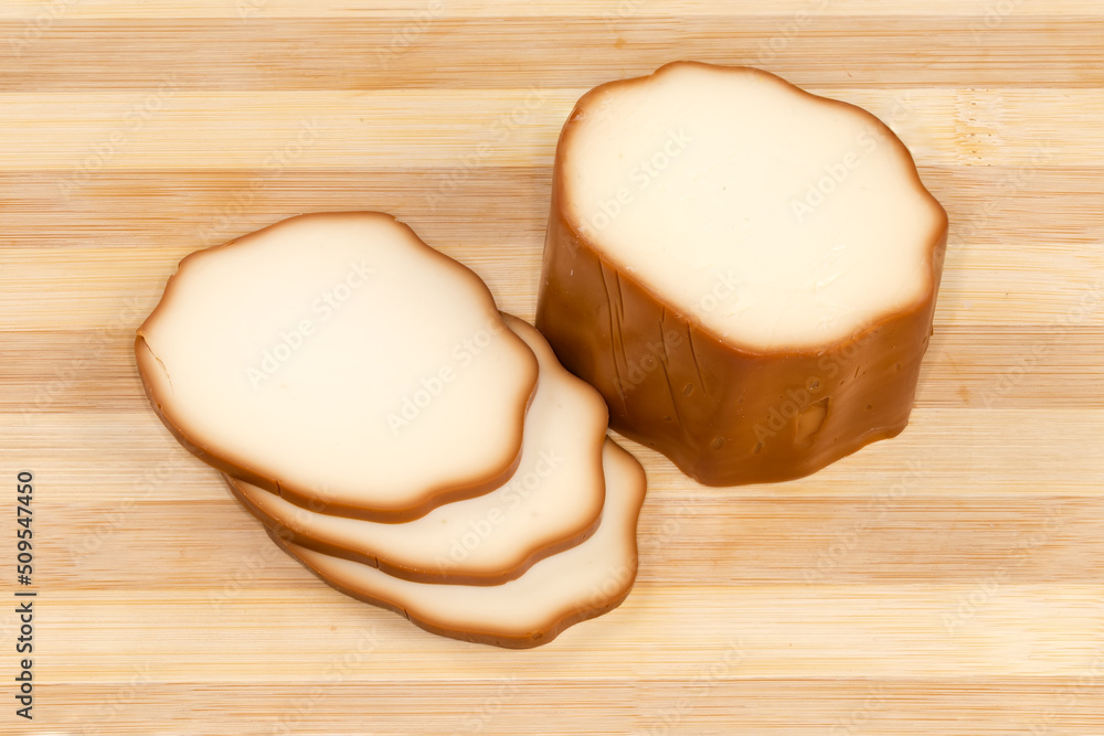 Partly sliced smoked processed cheese on a wooden cutting board Partly sliced smoked processed cheese on a wooden cutting board