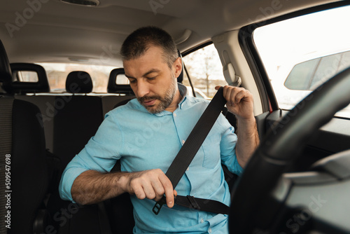 Male Driver Putting On Seat Belt Sitting In Automobile
