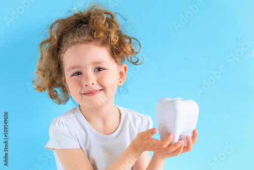 Little cute smiling girl holding tooth dent in hand. Kid training oral hygiene. creative medical dentistry. Child learning brushing, cleaning teeth. Prevention of caries in children. dental care kids photo