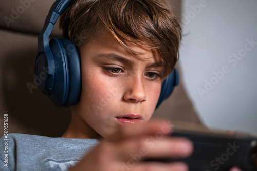 Portrait of enthusiastic young boy in headphones and holds mobile phone.