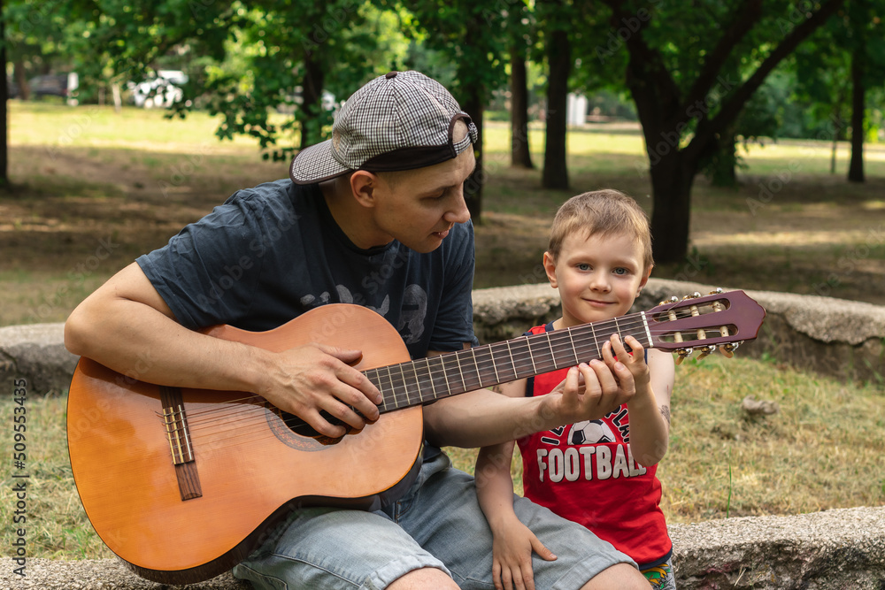 father teaching his son to play the guitar outside