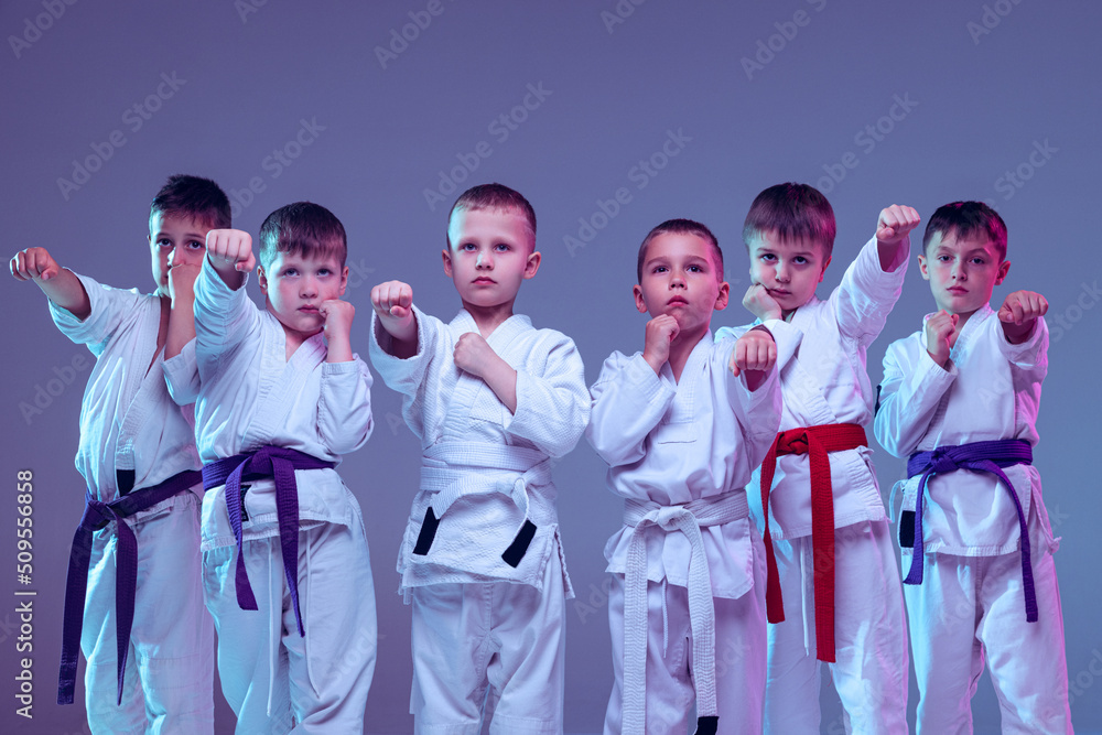 Group of kids, different boys, taekwondo athletes in white doboks in action isolated on lilac color background. Concept of sport, martial arts, education Group of kids, different boys, taekwondo athletes in white doboks in action isolated on lilac color background. Concept of sport, martial arts, education