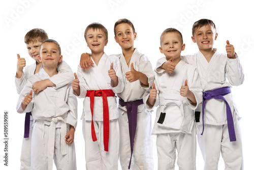 Group of happy children, beginner karate fighters in white doboks standing together isolated on white background. Concept of sport, martial arts, education photo