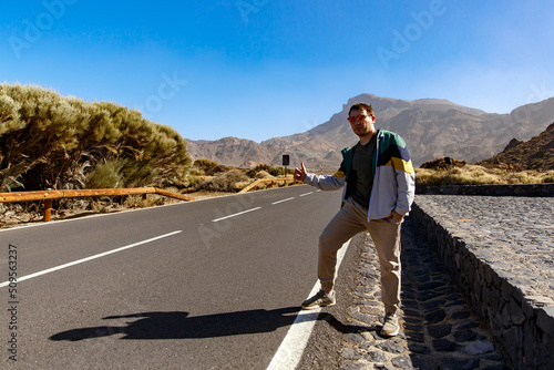 A hitchhiker stands near the road with a raised finger. Hitchhiking in mountains area.