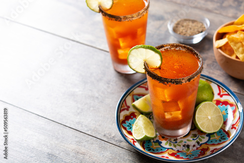 Homemade michelada cocktail with beer, lime juice,hot sauce,salted rim and tomato juice on wooden table. Copy space