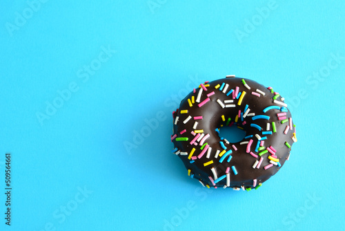 glazed chocolate doughnut with blue, pink, yellow and green sprinkles isolated on blue background