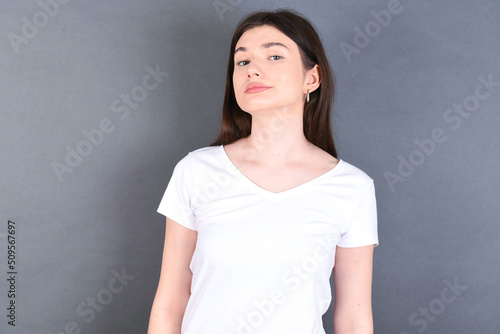 young beautiful Caucasian woman wearing white T-shirt over studio grey wa with snobbish expression curving lips and raising eyebrows, looking with doubtful and skeptical expression, suspect and doubt.