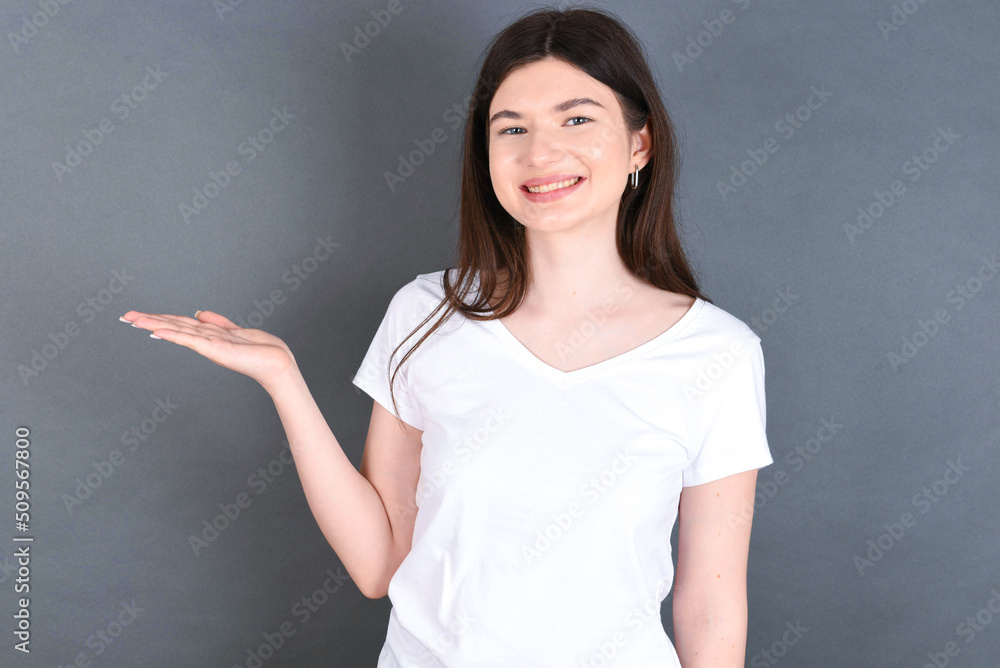 Positive glad young beautiful Caucasian woman wearing white T-shirt says: wow how exciting it is, has amazed expression, shows something on blank space with open hand. Advertisement concept. Positive glad young beautiful Caucasian woman wearing white T-shirt says: wow how exciting it is, has amazed expression, shows something on blank space with open hand. Advertisement concept.