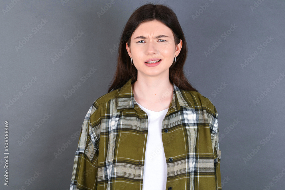 Portrait of dissatisfied young beautiful Caucasian woman wearing plaid shirt over studio grey wall smirks face, purses lips and looks with annoyance at camera, discontent hearing something unpleasant Portrait of dissatisfied young beautiful Caucasian woman wearing plaid shirt over studio grey wall smirks face, purses lips and looks with annoyance at camera, discontent hearing something unpleasant