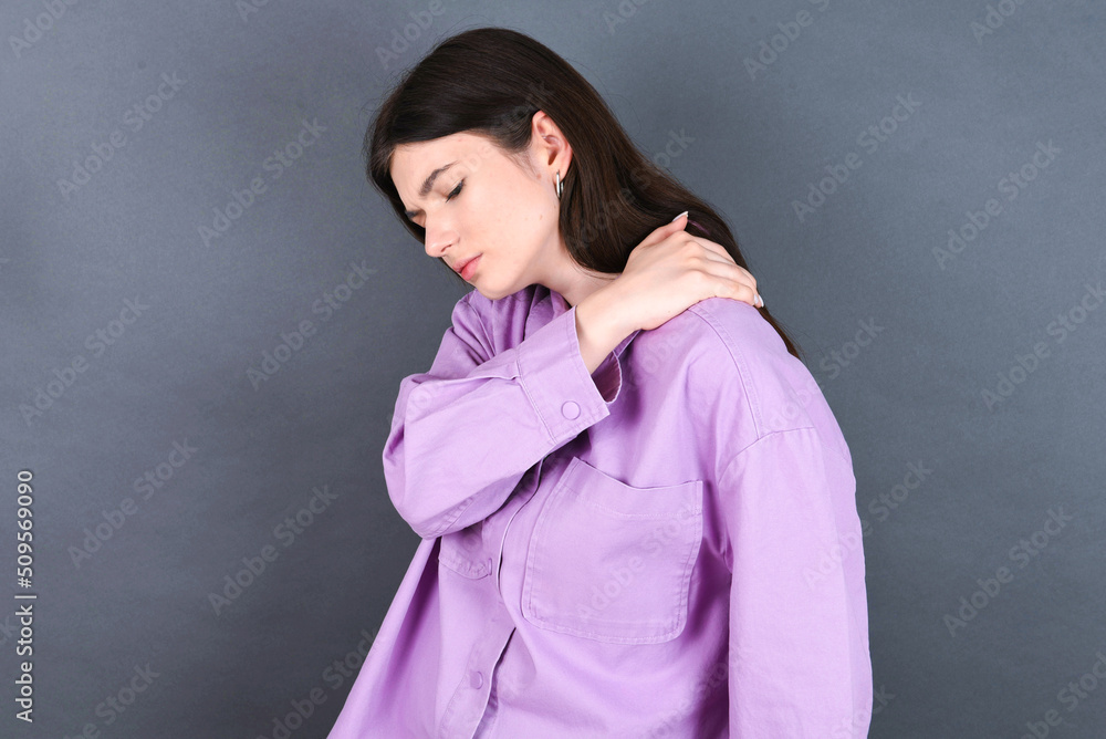 young beautiful Caucasian woman wearing pink shirt over studio grey wall got back pain young beautiful Caucasian woman wearing pink shirt over studio grey wall got back pain