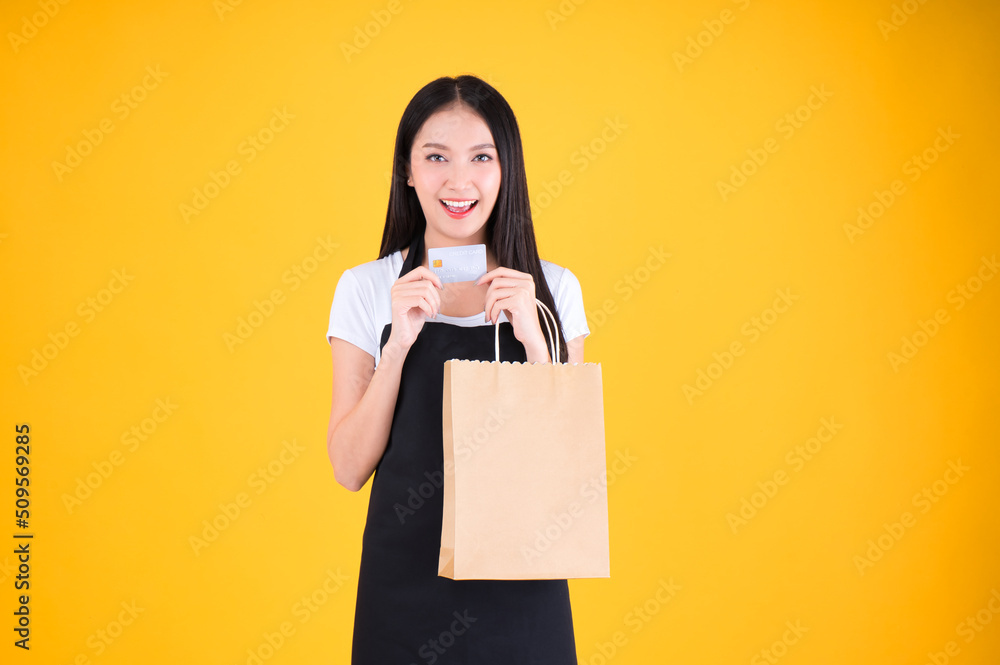 asian female smile wearing black apron holding paper bag and payment with a credit card through terminal money swiping a credit card asian female smile wearing black apron holding paper bag and payment with a credit card through terminal money swiping a credit card