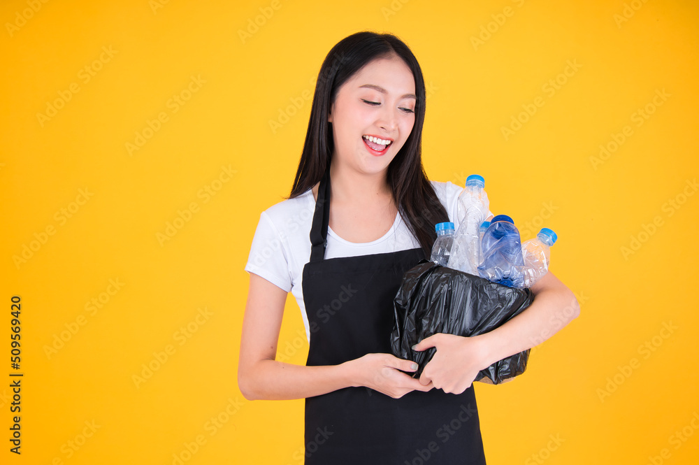 attractive asian female smile wearing apron pointing fingers to plastic bottle in a garbage bag for Recycling, world environment day. attractive asian female smile wearing apron pointing fingers to plastic bottle in a garbage bag for Recycling, world environment day.
