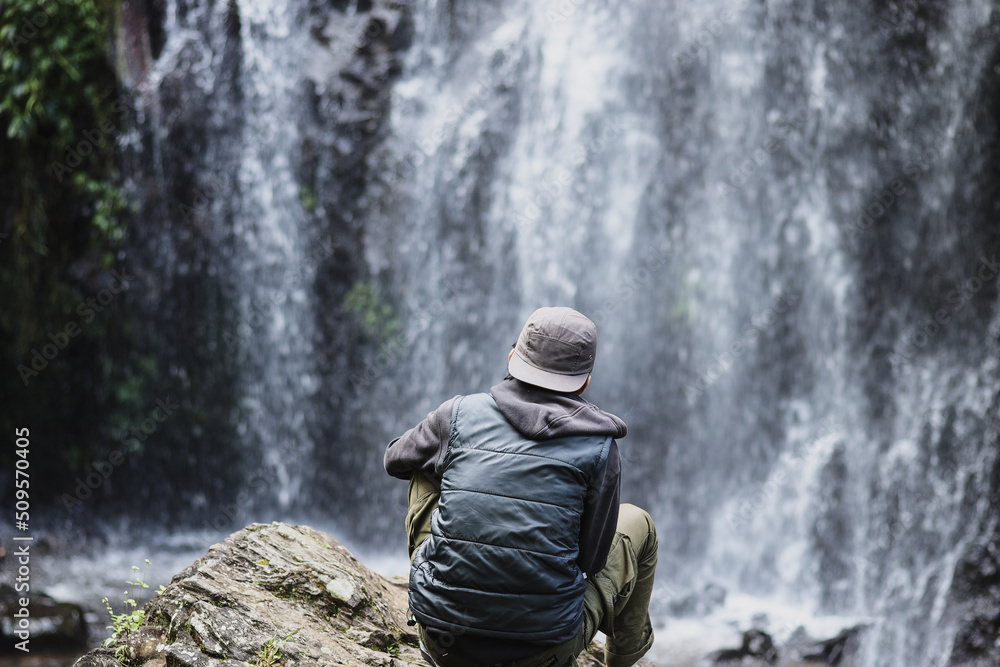 Back side of young Asian man in front of waterfall Back side of young Asian man in front of waterfall