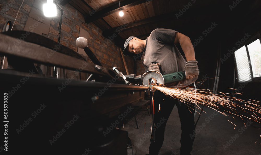 Fototapeta premium A man works with an angle grinder in his home workshop. Making metal products with your own hands