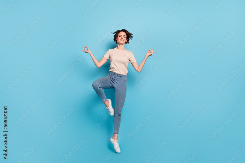 Full length photo of dreamy cute woman wear beige t-shirt jumping high practicing yoga isolated blue color background