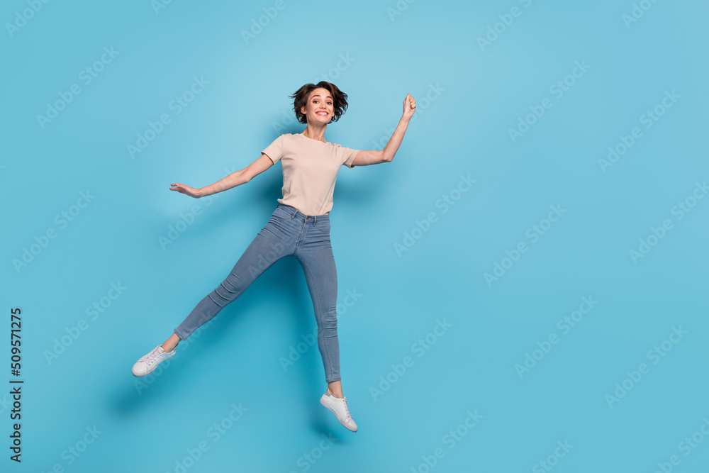 Fototapeta premium Full length photo of sweet pretty woman wear beige t-shirt jumping high empty space isolated blue color background
