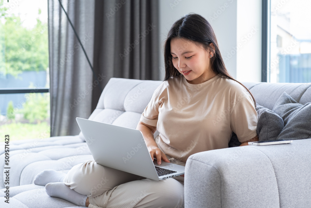beautiful young asian woman in casual cozy clothes using laptop sitting on couch at modern apartment beautiful young asian woman in casual cozy clothes using laptop sitting on couch at modern apartment