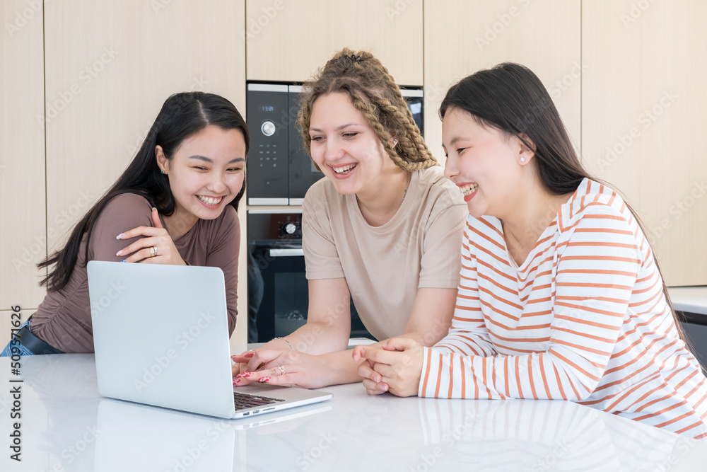 young carefree diversity women friends using laptop, having fun together at modern kitchen at home