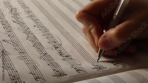 Handwritten notes and female hand holding a pen and writing notes, composing music, selective focus