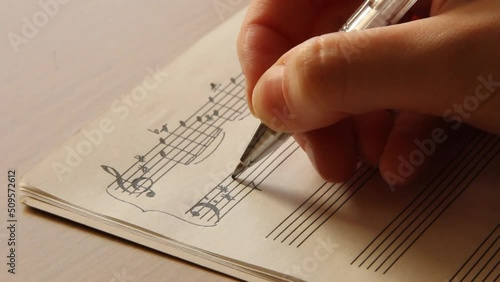 Handwritten notes and female hand holding a pen and writing notes, composing music, selective focus