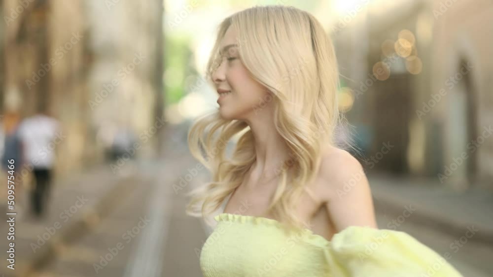 Smiling woman walking down the city street. Flirty girl with long blond hair turning around in city centre. Smiling woman walking down the city street. Flirty girl with long blond hair turning around in city centre.