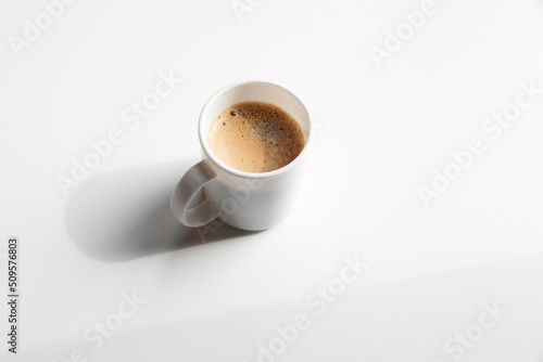 Cup of fresh crema espresso with bubble and froth on white empty table or background.