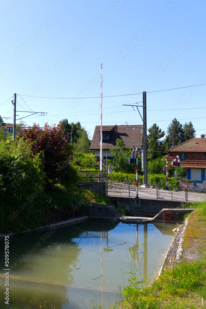 Pond with grass, hedges and trees with open railway barrier in the background on a sunny spring day at City of Zürich. Photo taken May 18th, 2022, Zurich, Switzerland.