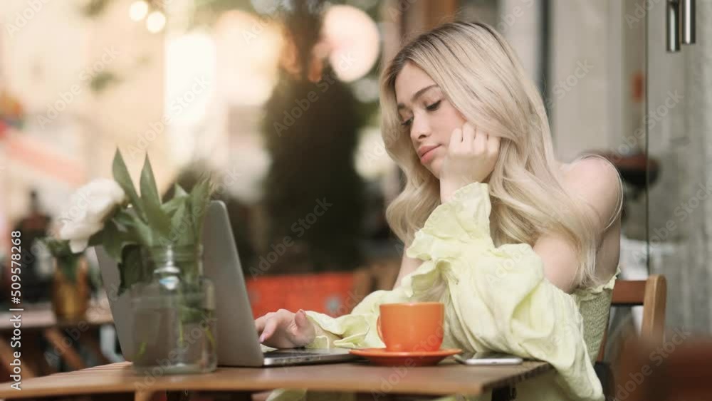 Close up view of tired exhausted boring young woman typing on laptop and falls asleep while sitting with a laptop at cafe. Close up view of tired exhausted boring young woman typing on laptop and falls asleep while sitting with a laptop at cafe.