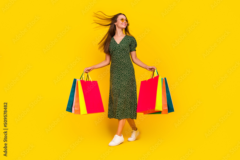 Full size portrait of cheerful lovely girl hold packages flying hairstyle isolated on yellow color background