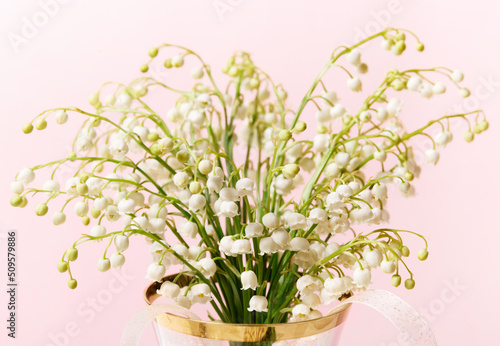 Delicate romantic bouquet of small white lilies of the valley on pink background.