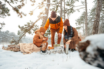 Happy family with cups of hot tea spending time together in winter forest