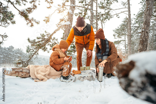 Happy family with cups of hot tea spending time together in winter forest Fototapet
