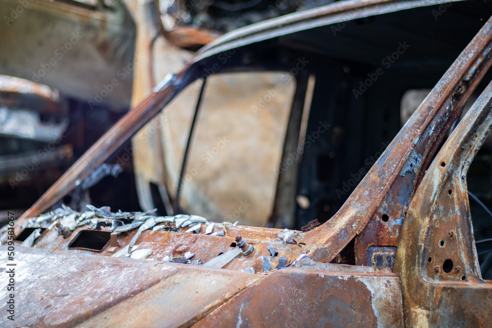 The car was completely destroyed by fire. Abandoned, burnt and rusty car by the road. Cars were on fire in the parking lot. War of Russia against Ukraine. Shrapnel and bullet holes in cars.