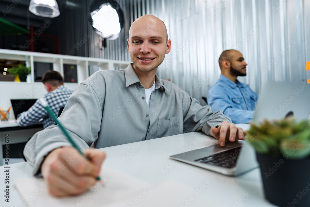 Obraz premium Young bald business man sitting at desk in office, working on computer