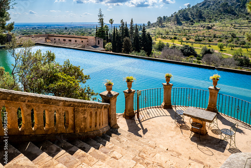 An old staircase leads down to a semicircular terrace with a stone table and four chairs that adjoins a big water reservoir, which irrigated the gardens of Raixa, a famous public Majorcan mansion.