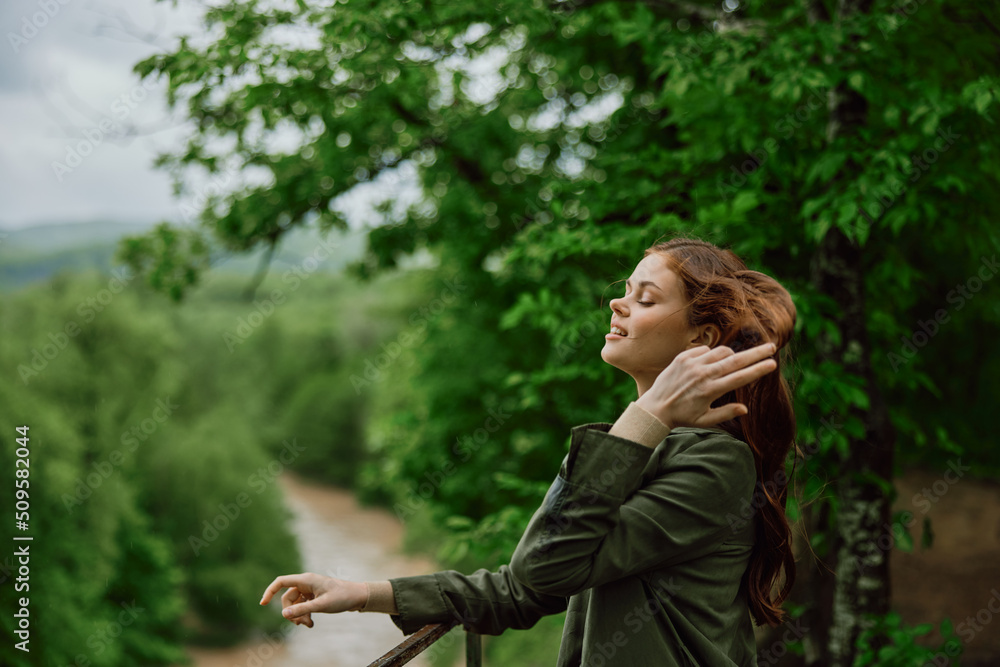 a beautiful woman with red hair blowing in the wind stands in a park overlooking a mountain river a beautiful woman with red hair blowing in the wind stands in a park overlooking a mountain river
