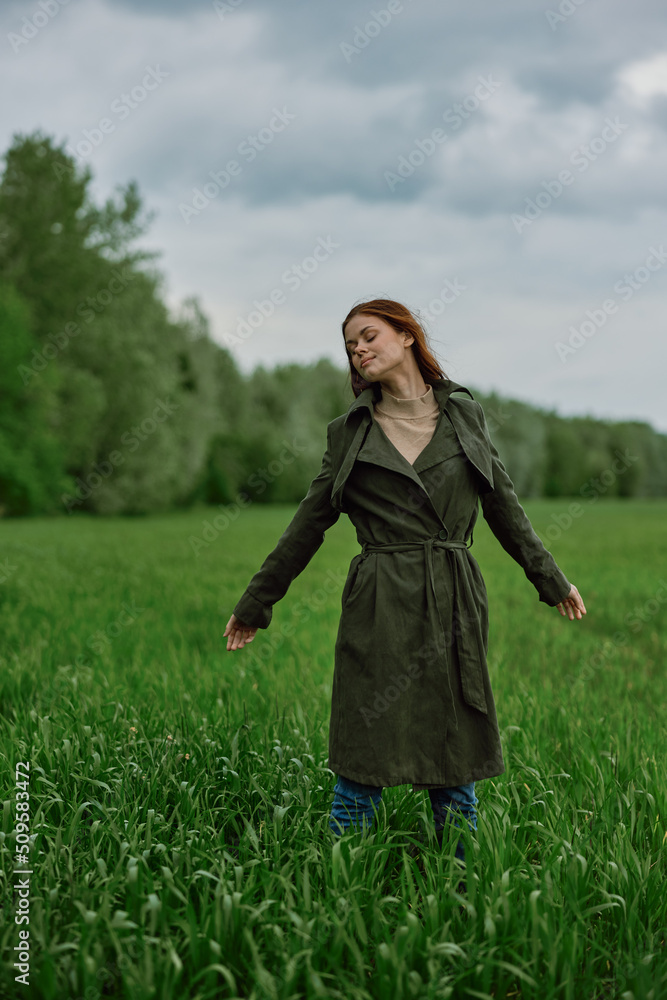 a beautiful woman stands in a field in a long raincoat enjoying nature a beautiful woman stands in a field in a long raincoat enjoying nature