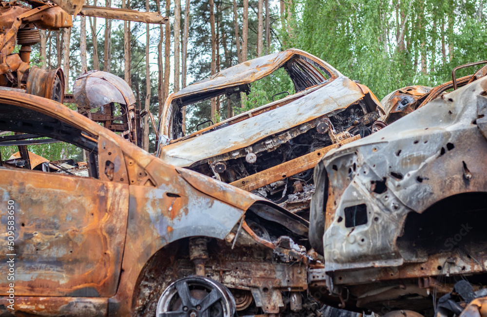 A view of burnt-out cars after rocket attacks by the Russian military. War of Russia against Ukraine. Civil vehicle after the fire. Cemetery of cars in the city of Irpin. Rusty pile of metal.